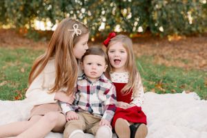 Three children sitting together on blanket in autumn setting.