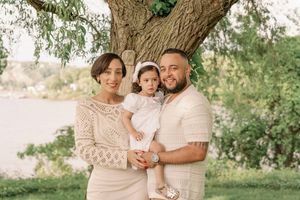 A group in coordinated beige and white outfits pose together outdoors in a natural garden setting during a sunny day.