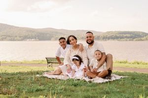 Family relaxes together on blanket in scenic mountain meadow during golden hour sunset.