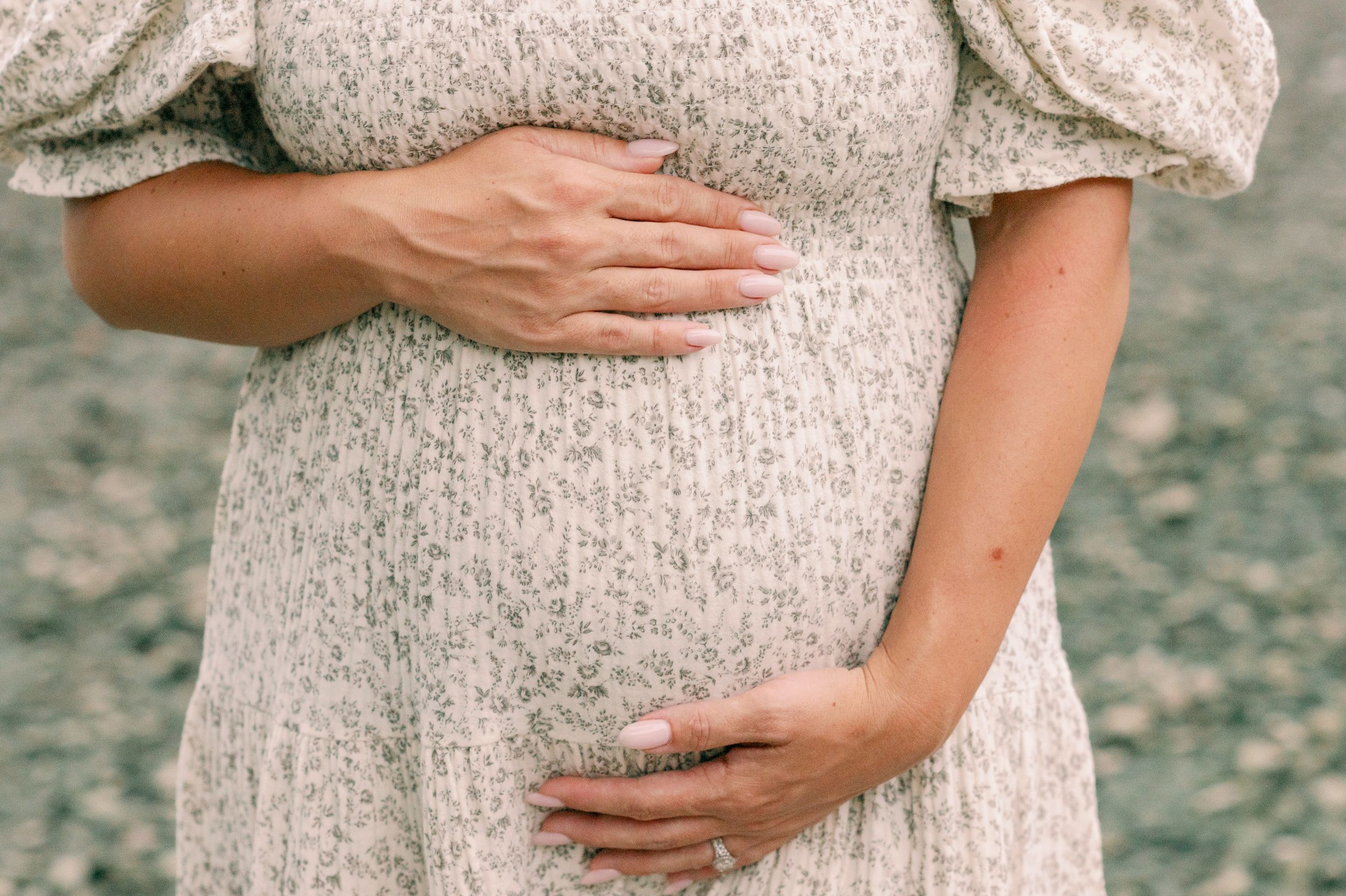 Close-up of hands cradling pregnant belly in lace dress.