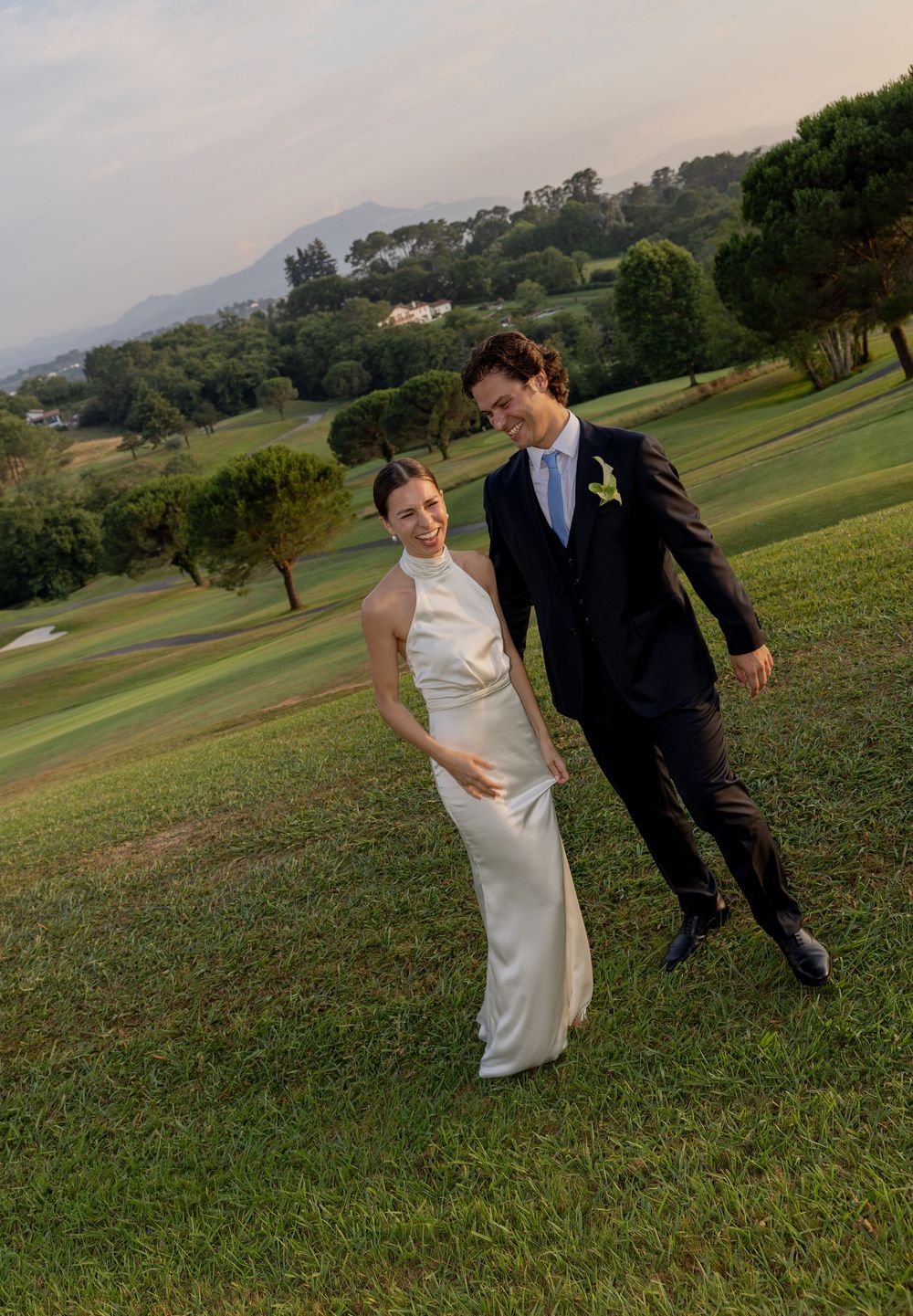 Newlyweds enjoy a romantic moment on a hillside golf course during golden hour.