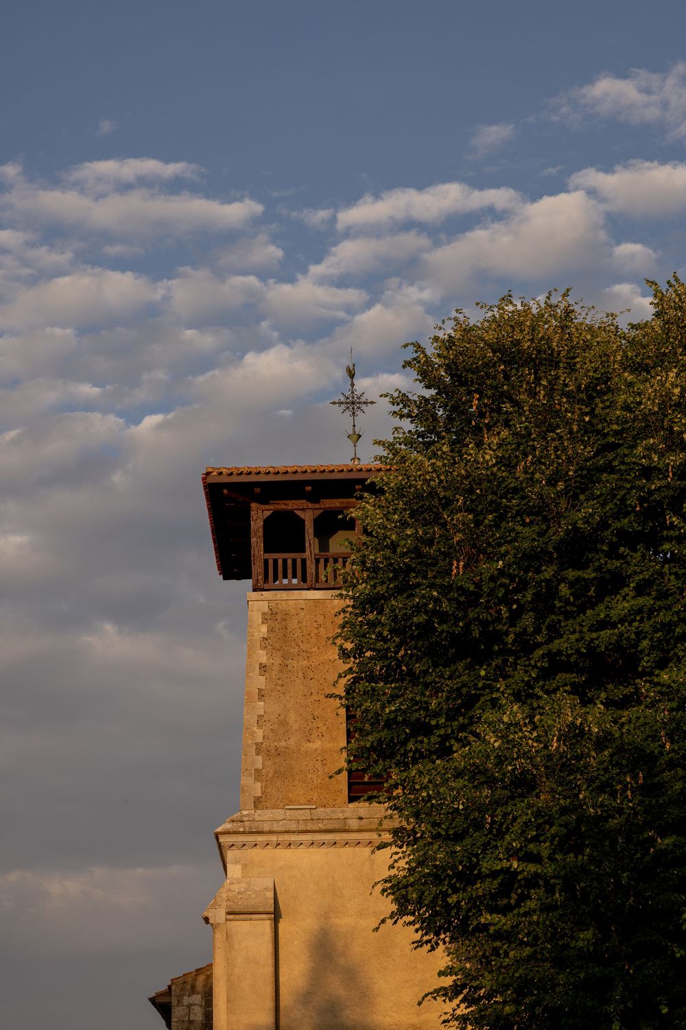 Stone church tower with a cross silhouetted against a cloudy blue sky during golden hour.