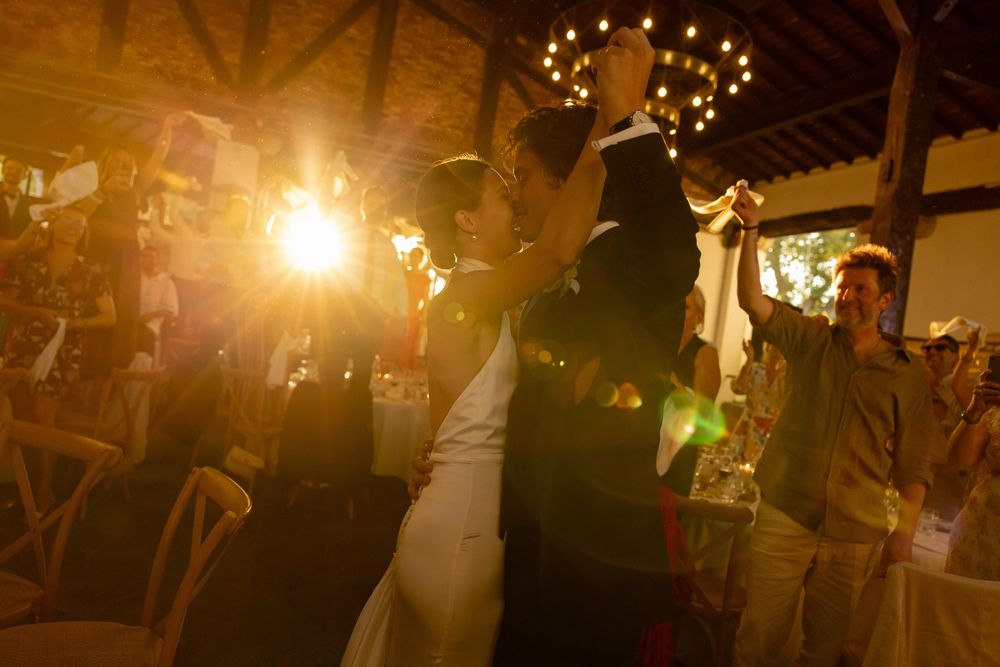 Wedding guests dancing and celebrating with arms raised under warm lighting at an evening reception.