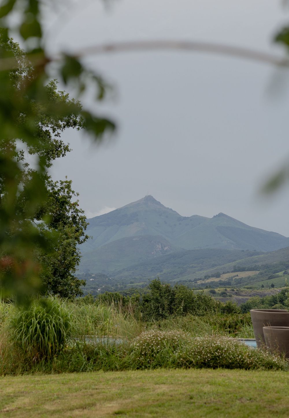 A majestic mountain peak rises above rolling green hills and trees in a peaceful countryside landscape.