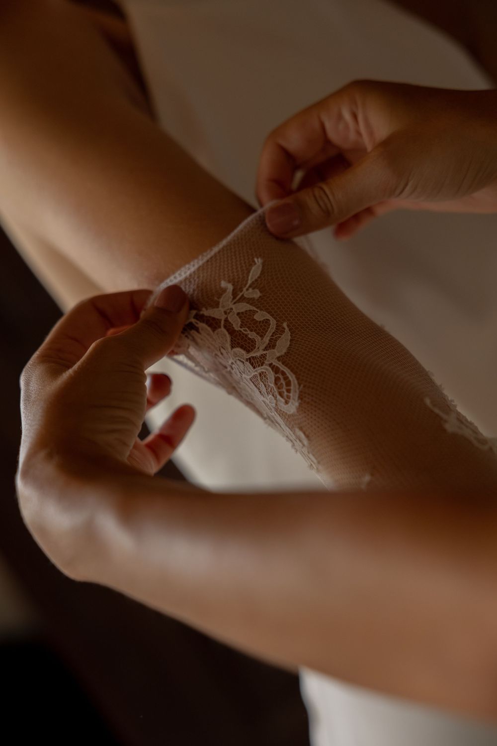 Delicate lace garter detail being adjusted on someone's leg in soft, intimate lighting.