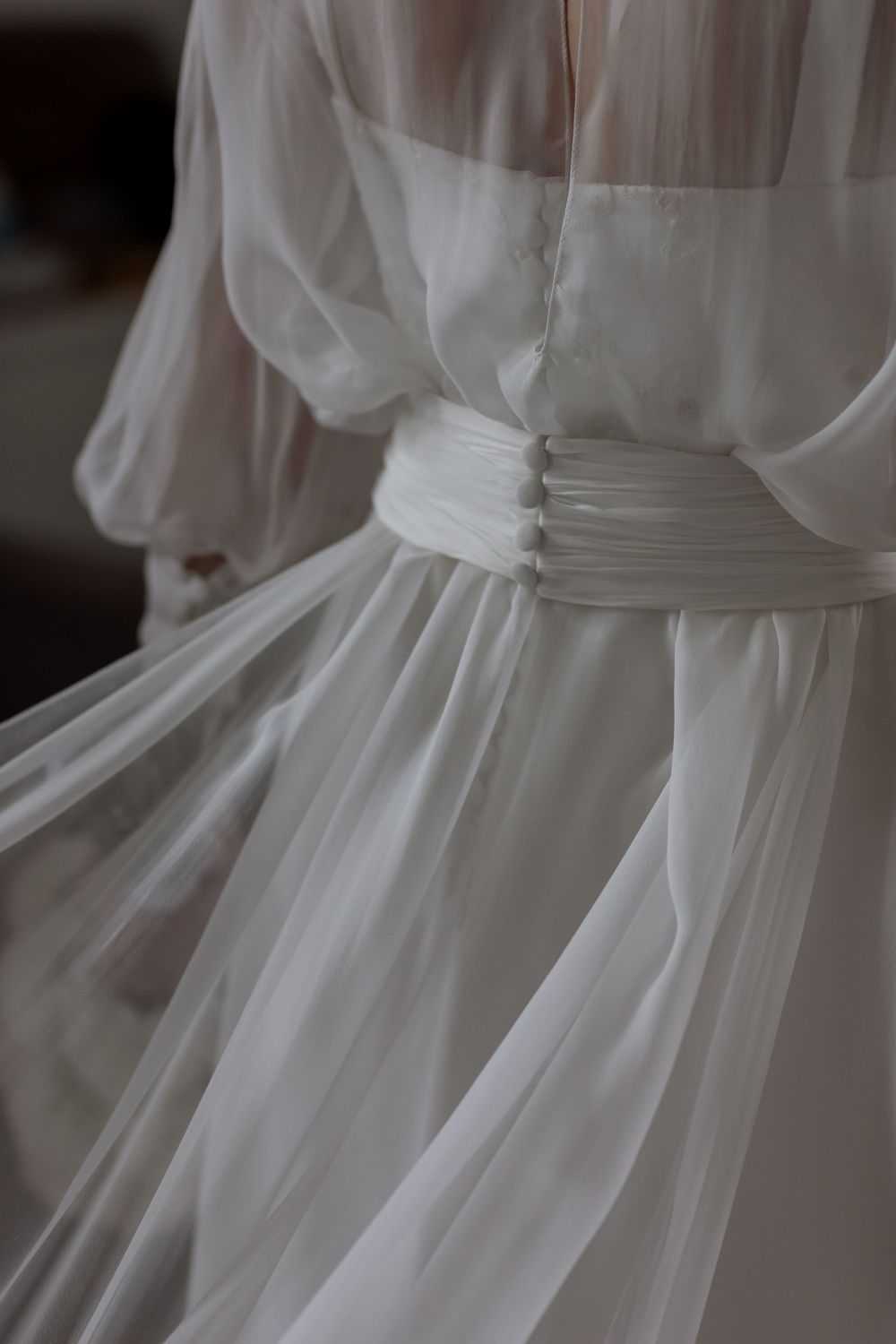 Close-up of an elegant white chiffon wedding dress with ruched satin waist belt and flowing sheer skirt.