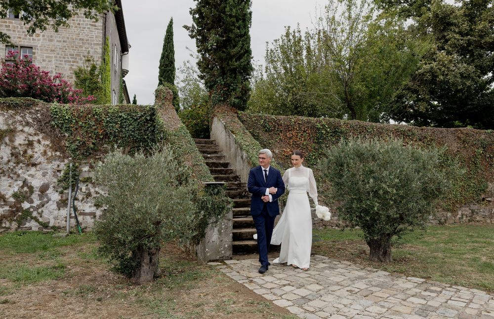 Bride and groom walk through a lush Italian garden with stone steps and cypress trees on their wedding day.