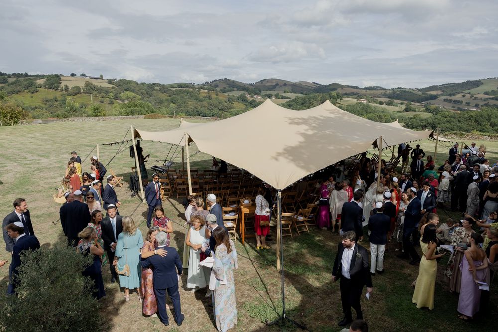 Outdoor wedding reception under a large stretch tent on a scenic Tuscan hillside with guests mingling.
