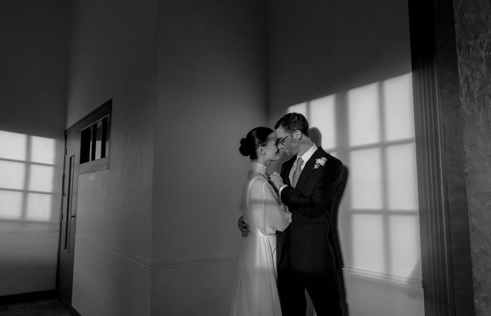 Black and white photo of a bride and groom sharing an intimate moment in a sunlit room.