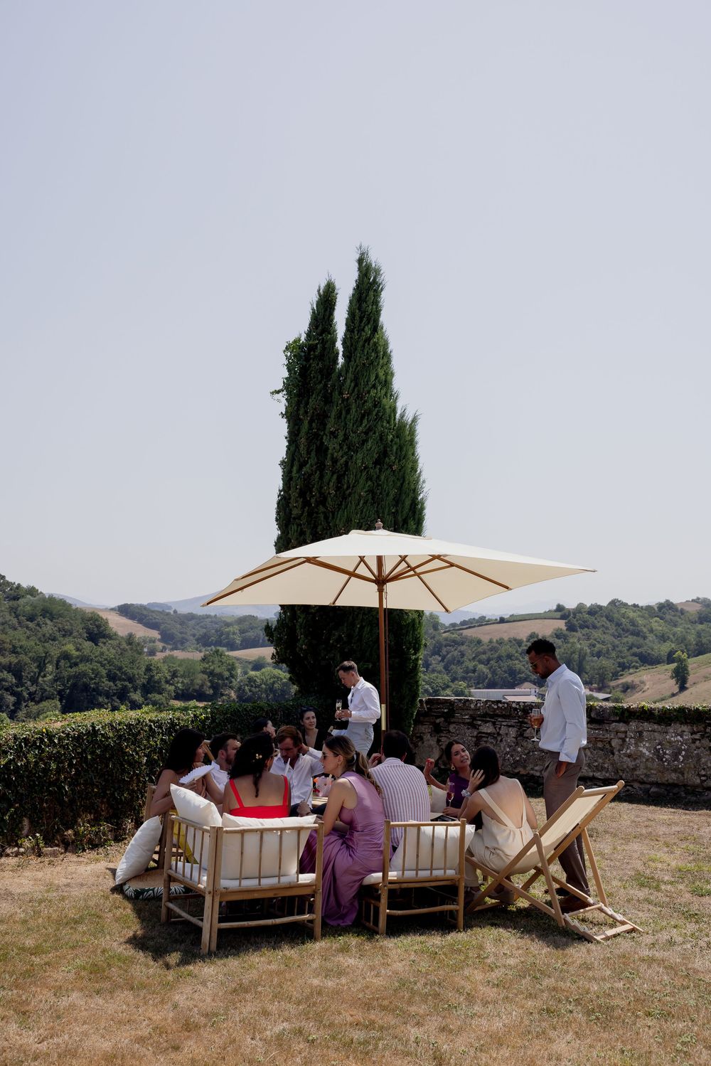 Group of guests gathered around an outdoor table with umbrella, enjoying a sunny day in the Tuscan countryside.
