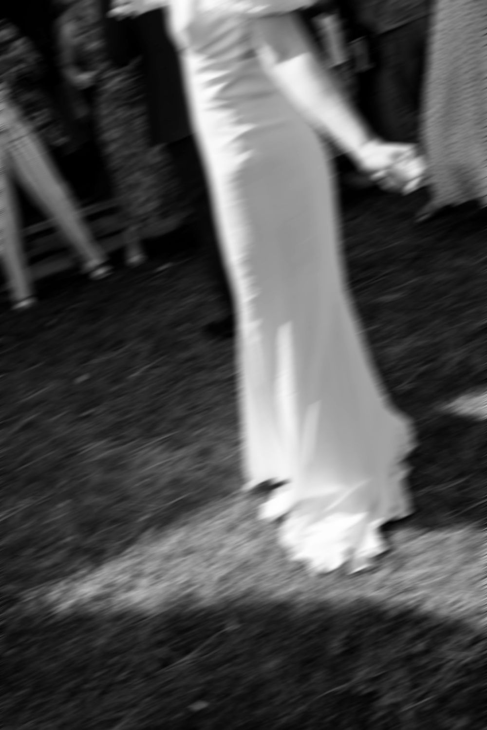 Blurry black and white photo of a bride in a white gown dancing outdoors at a wedding reception.