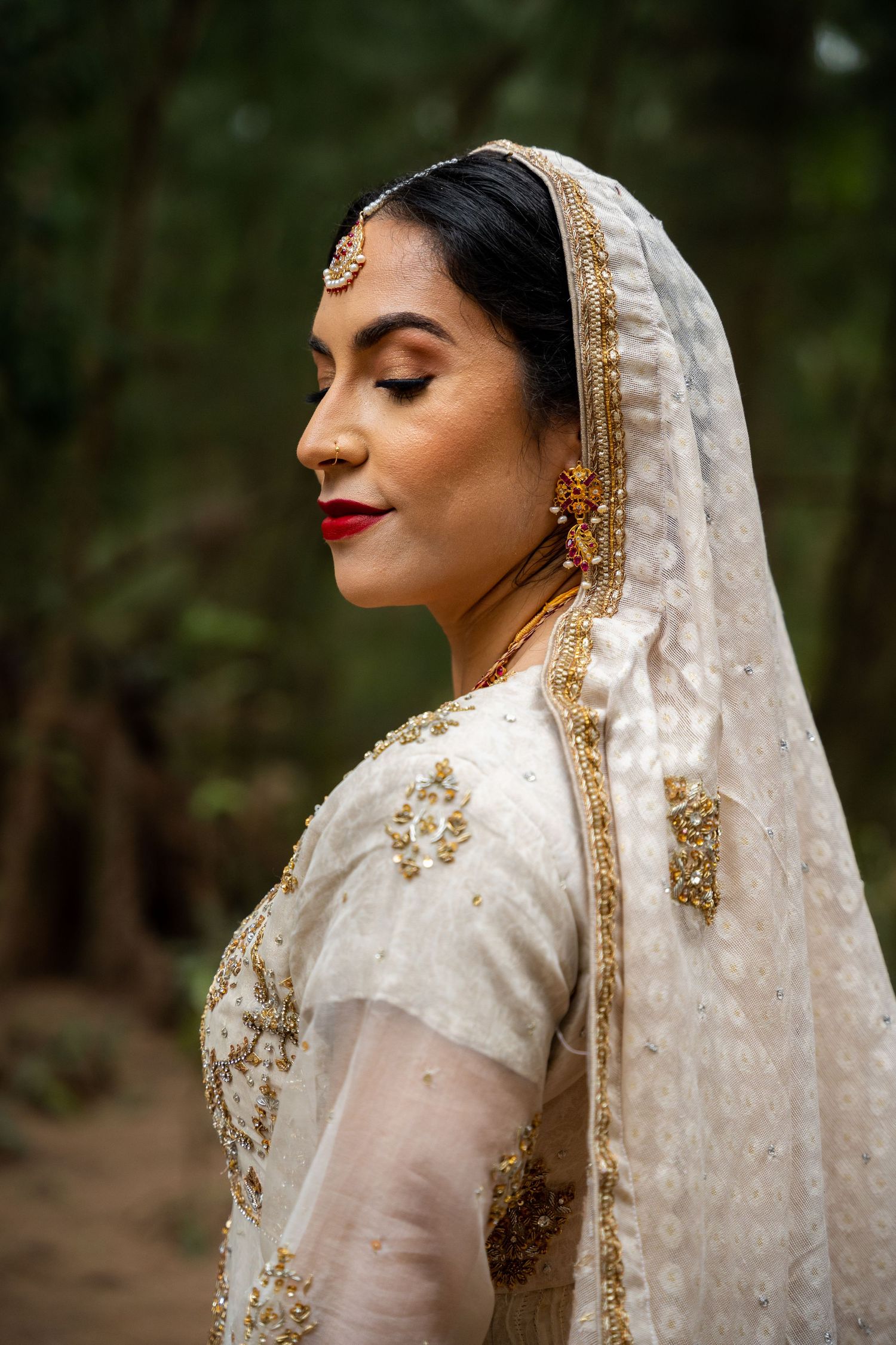 Close-up portrait of bride in traditional Indian attire with detailed gold embroidery and red lipstick.