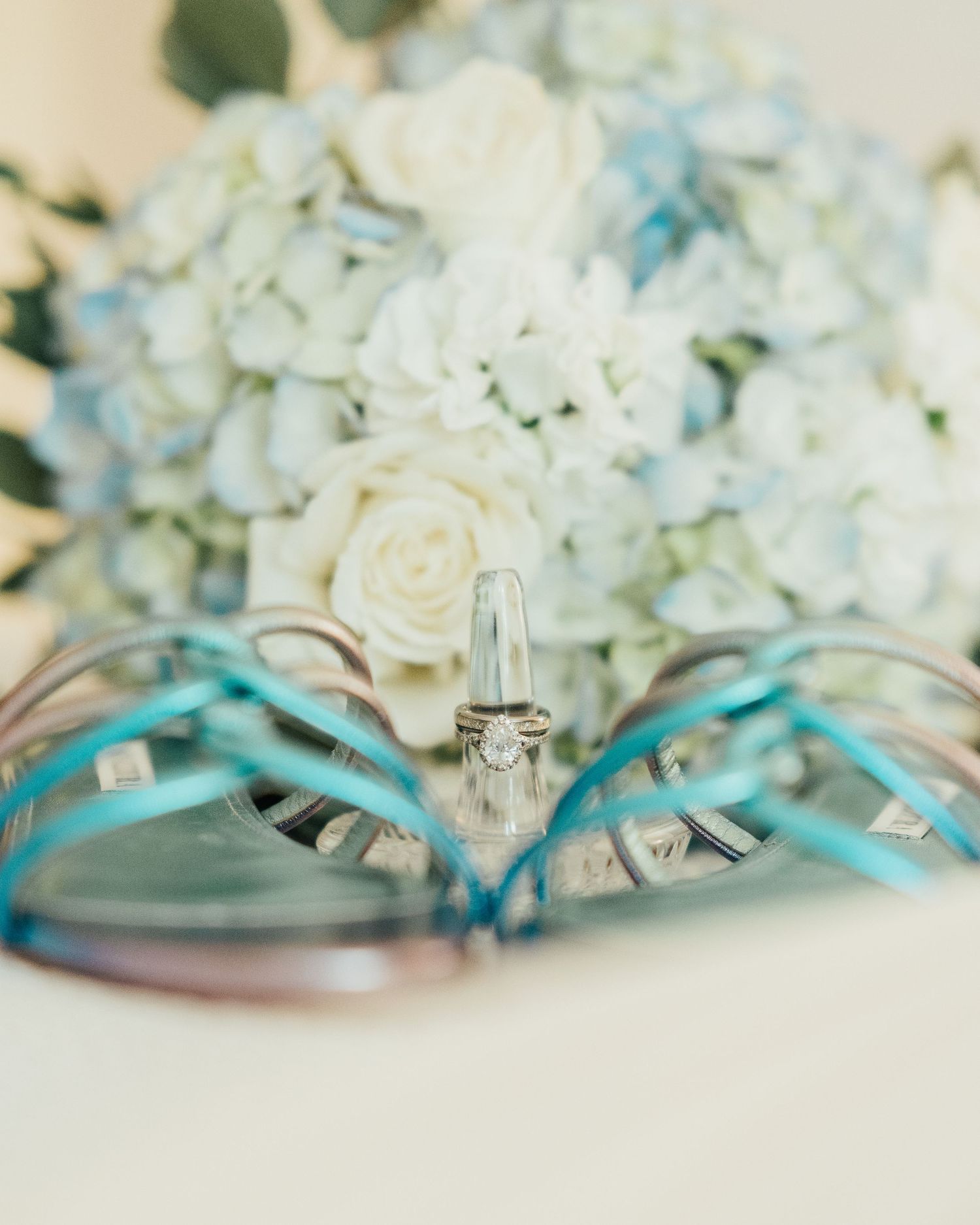 Wedding ring displayed with blue shoes and white hydrangea bouquet.