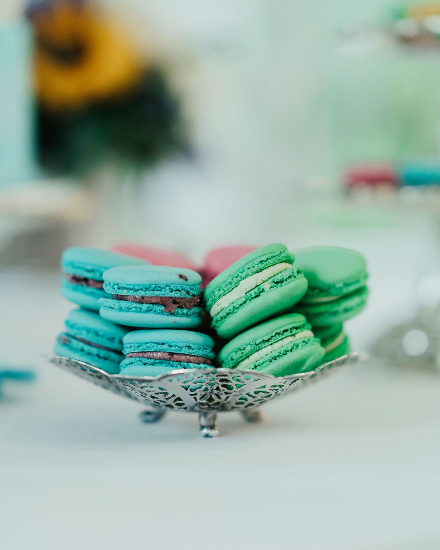 Colorful turquoise and pink macarons displayed on an ornate silver plate.