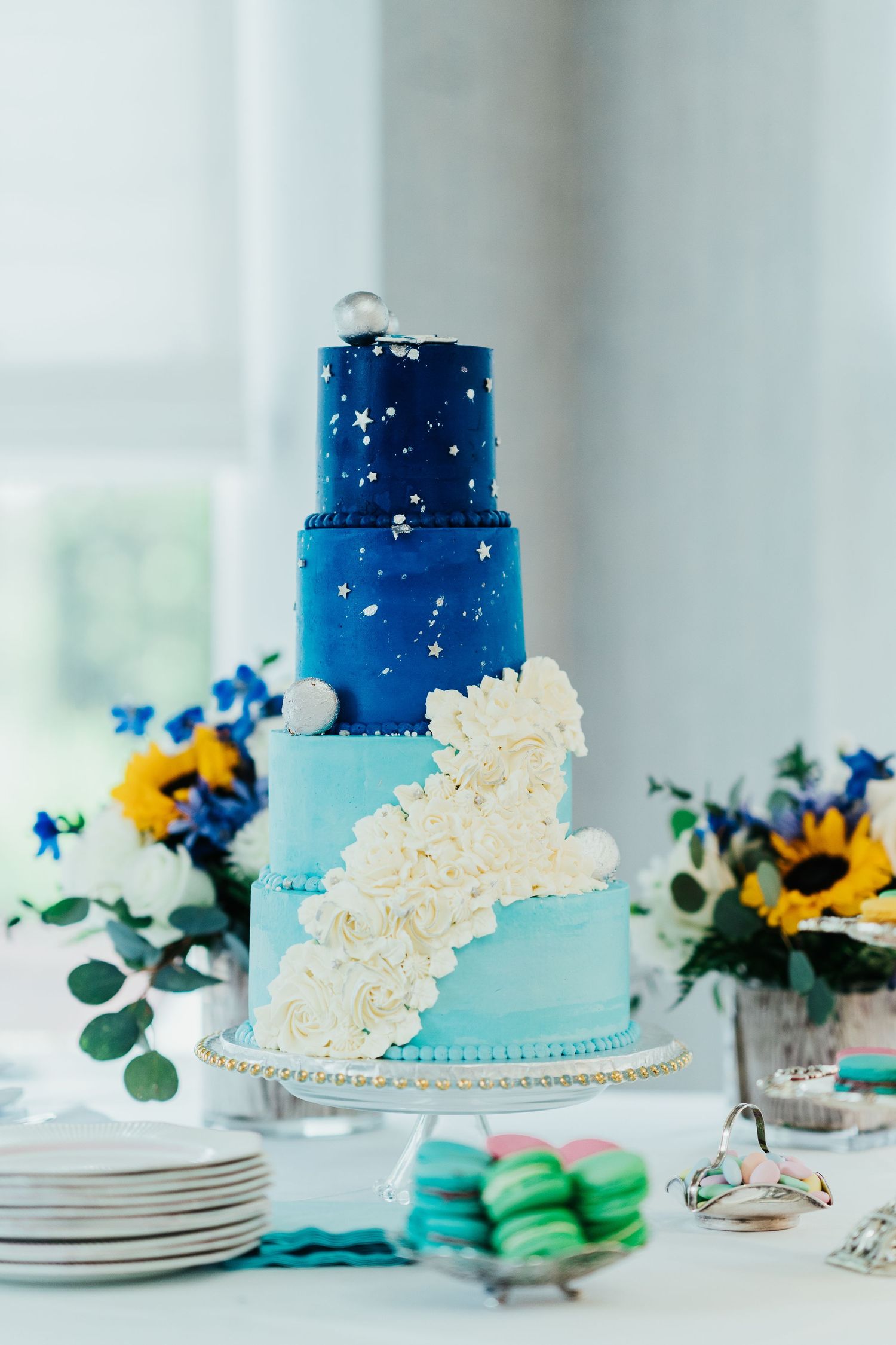 Three-tier blue ombre wedding cake decorated with stars and sunflowers.