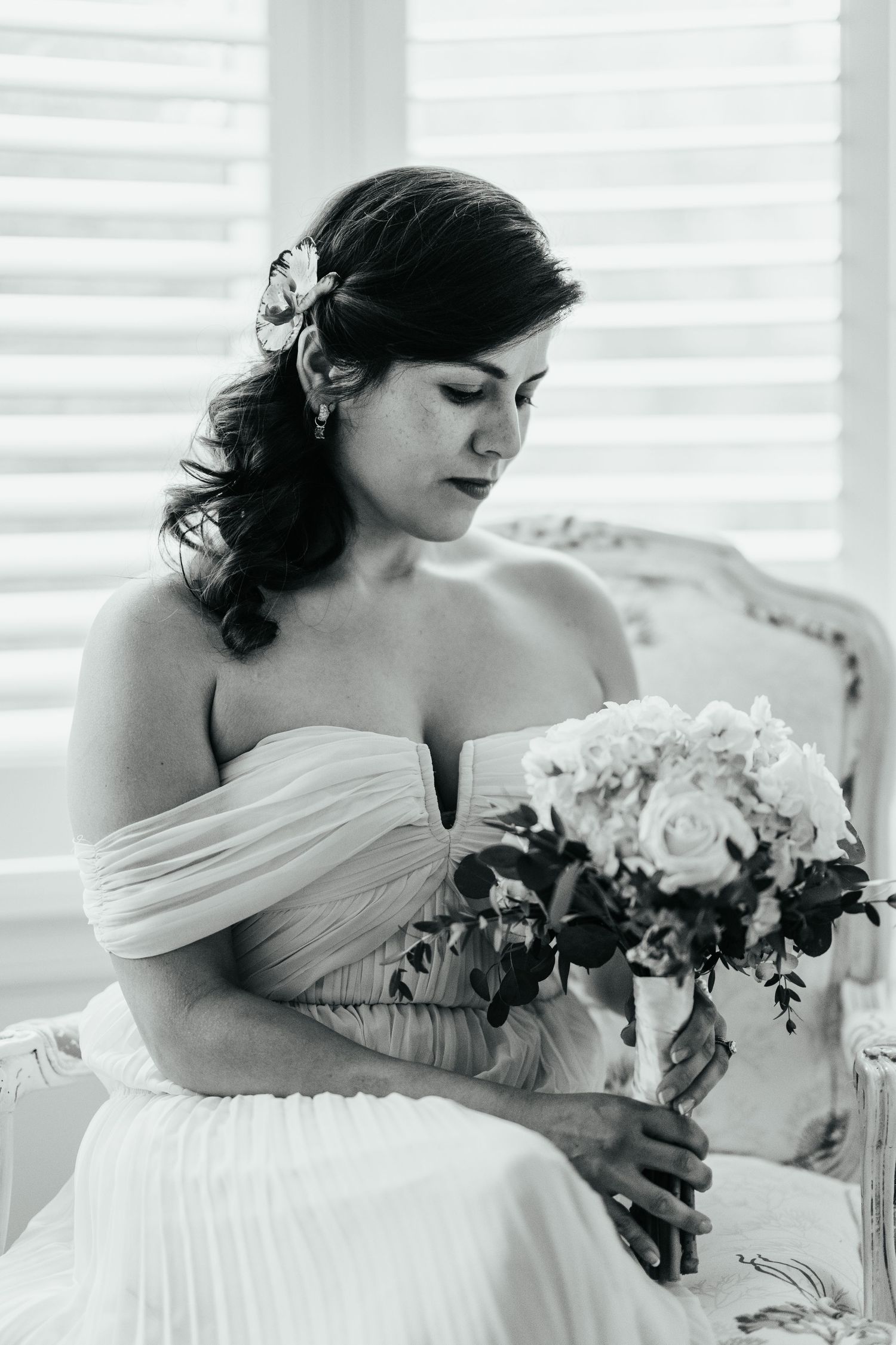 Black and white portrait of bride holding bouquet while seated in romantic vintage setting.