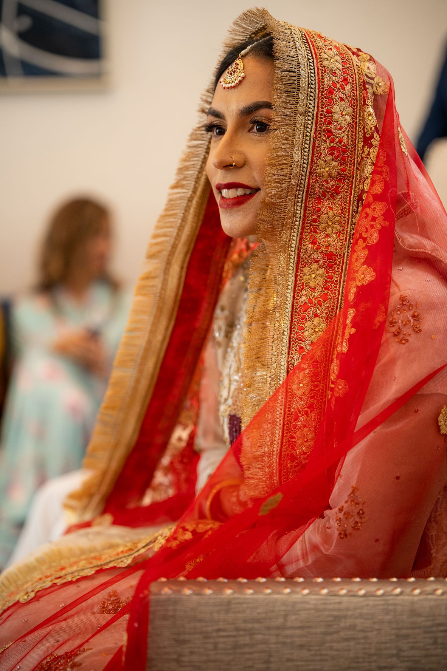 Traditional Indian bride wearing an ornate red and gold dupatta with intricate embroidery at a wedding celebration.