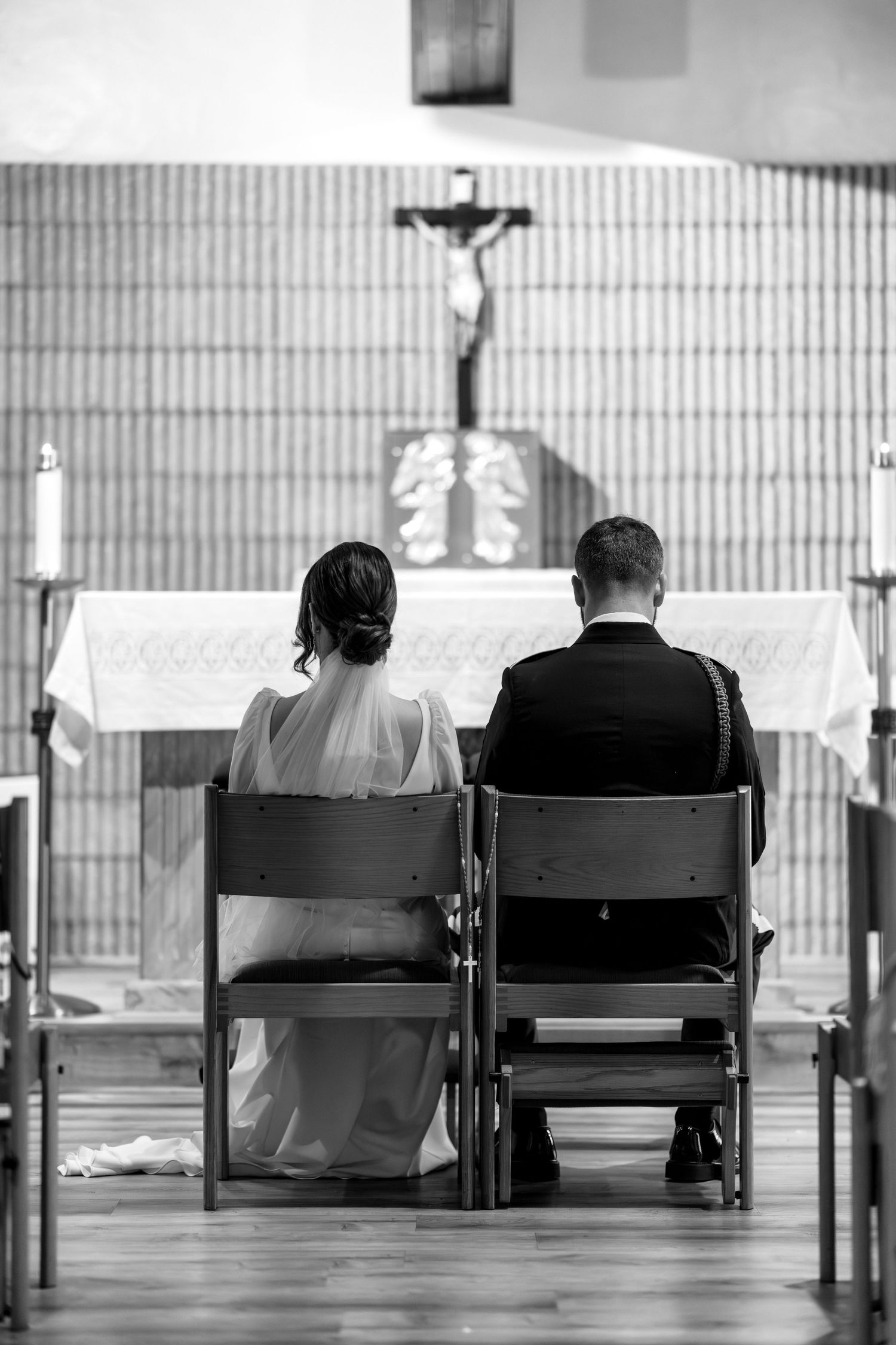 Back view of couple sitting in church chairs facing altar during ceremony.