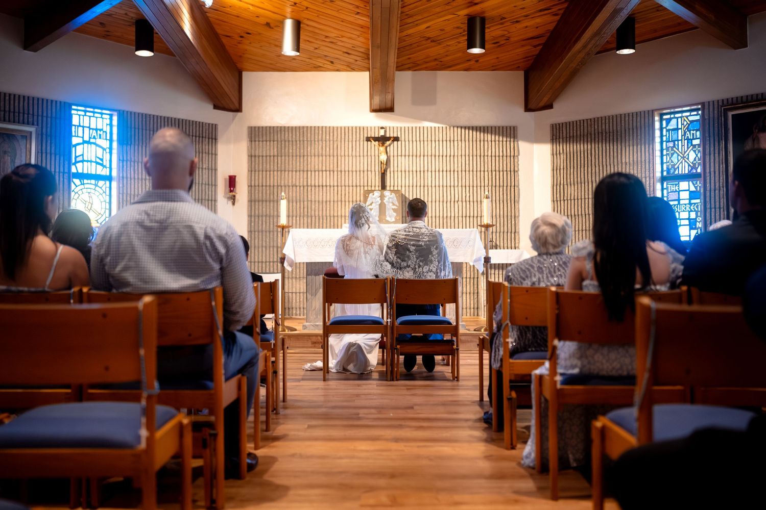 Interior of church sanctuary during wedding ceremony with wooden pews and crucifix.
