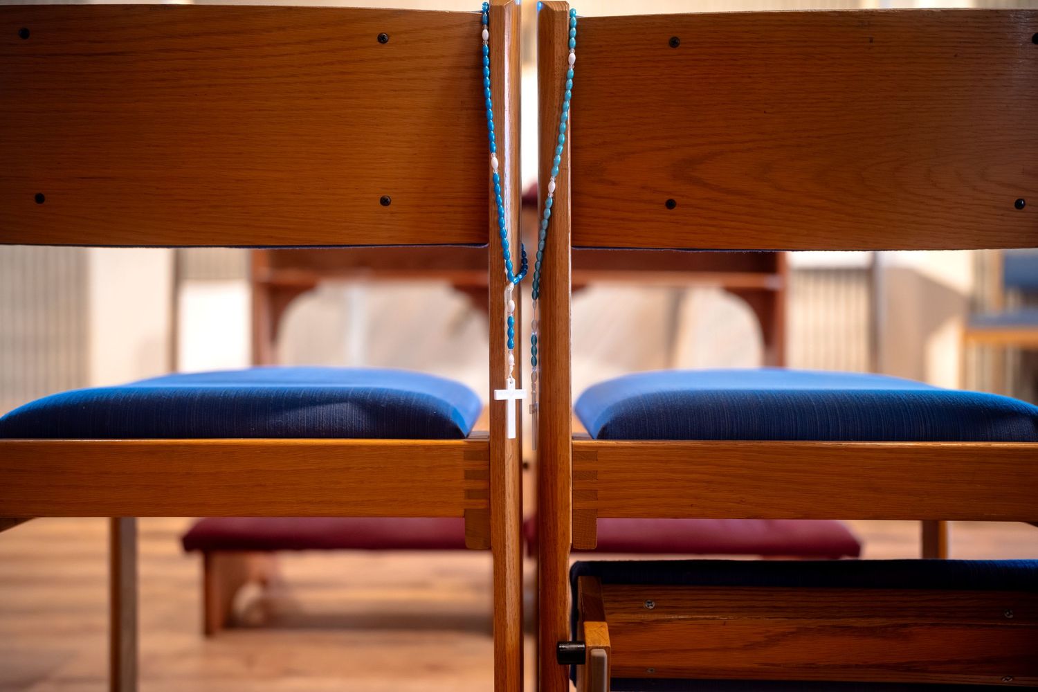 Close-up of wooden church pews with blue cushioned seats in sanctuary.
