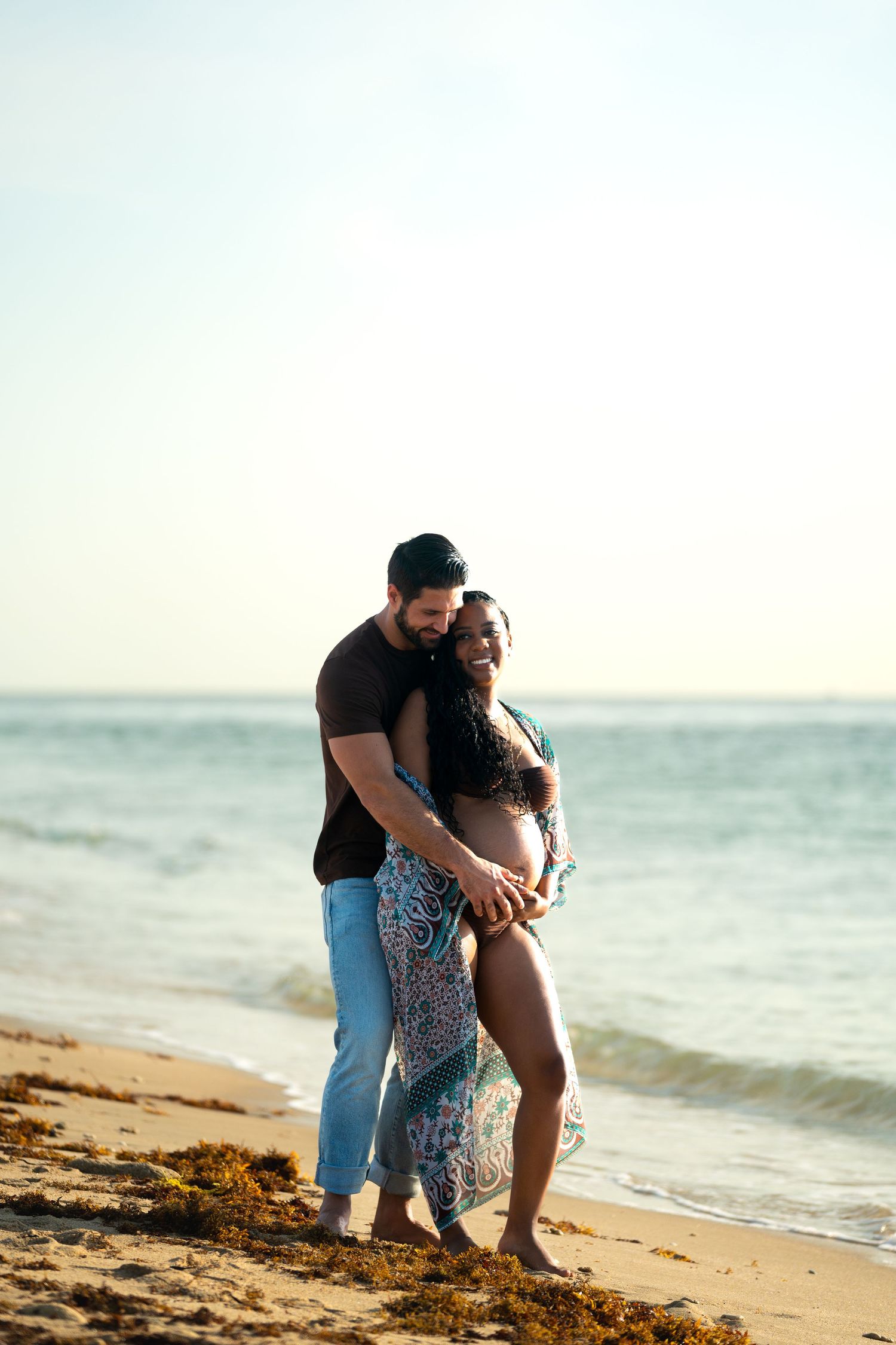A couple shares an intimate moment together on a beach at sunset.