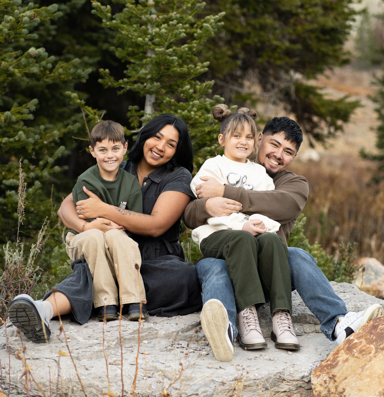 A beautiful family of four embracing in the forest in Tony's grove in logan canyon during a fall family session with fall colors.