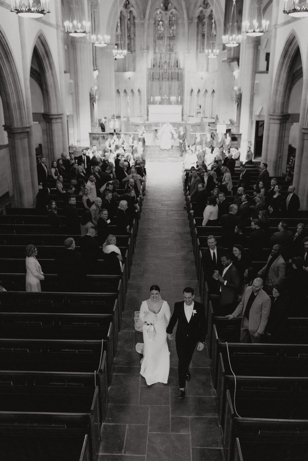 Black and white aerial view of a bride and groom walking down the aisle of an elegant church.