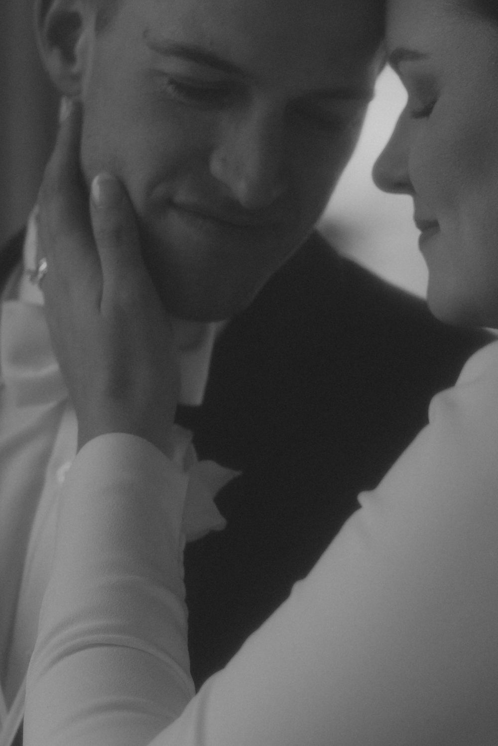 Black and white photo of a bride tenderly touching her groom's face in an intimate wedding moment.