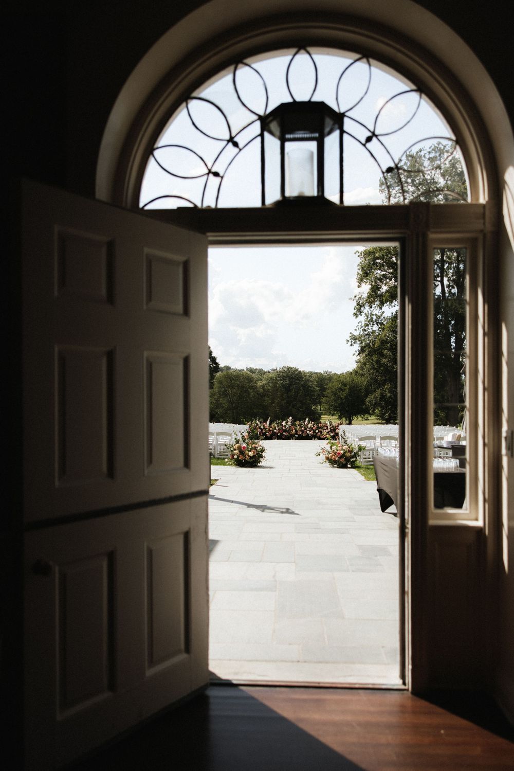 Elegant arched doorway opens to an outdoor wedding ceremony setup with floral arrangements.