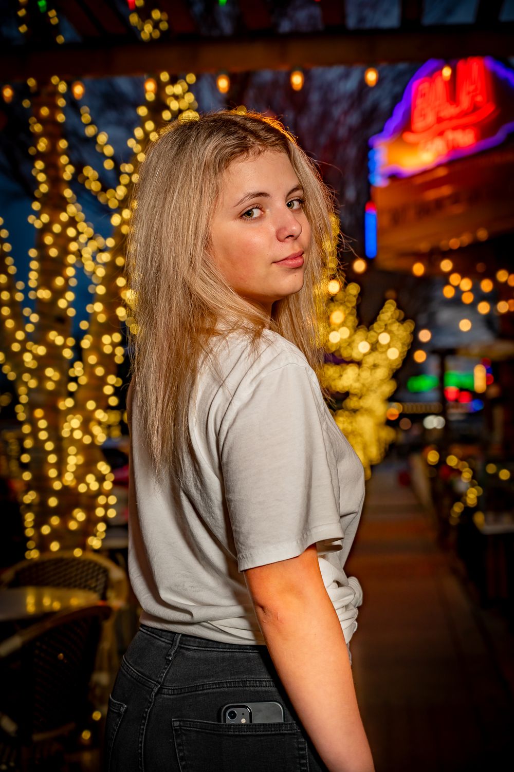 Night portrait with festive string lights and neon signs creating colorful bokeh background.