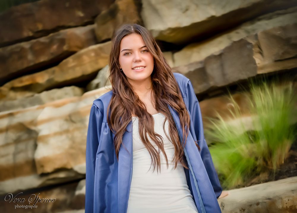 Casual senior portrait against rocky backdrop in blue cardigan and white dress.