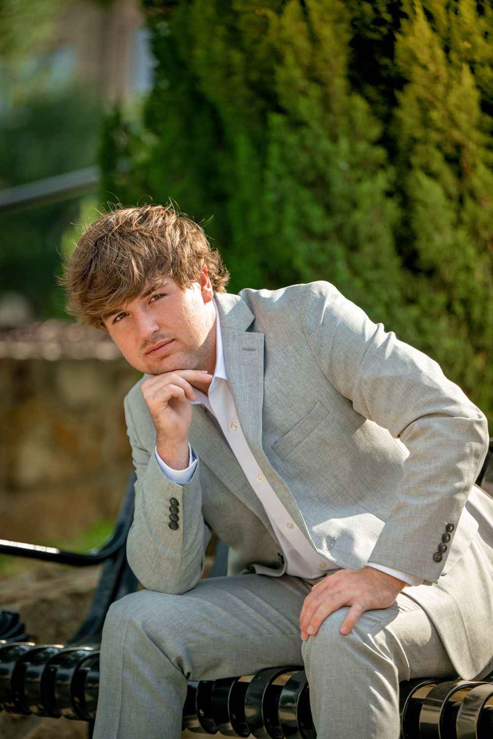 Stylish senior portrait of person in light gray suit sitting thoughtfully on bench.