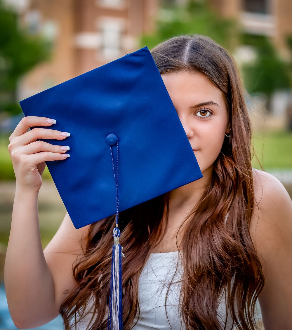 Graduation photo highlighting blue cap covering half the face against brick background.