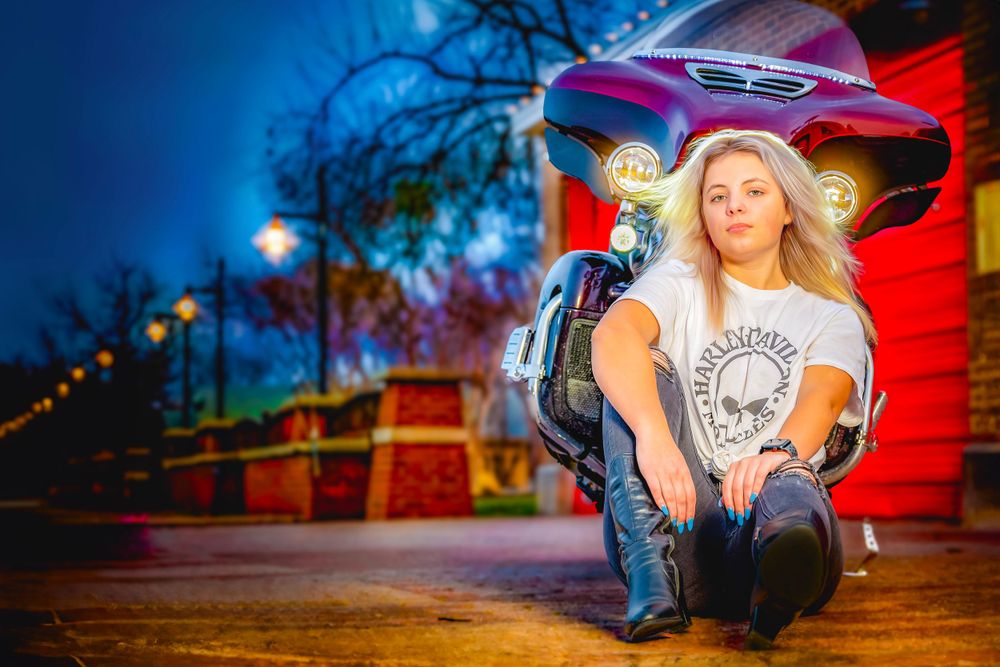Artistic senior portrait at dusk featuring a casual outfit against vibrant red background.