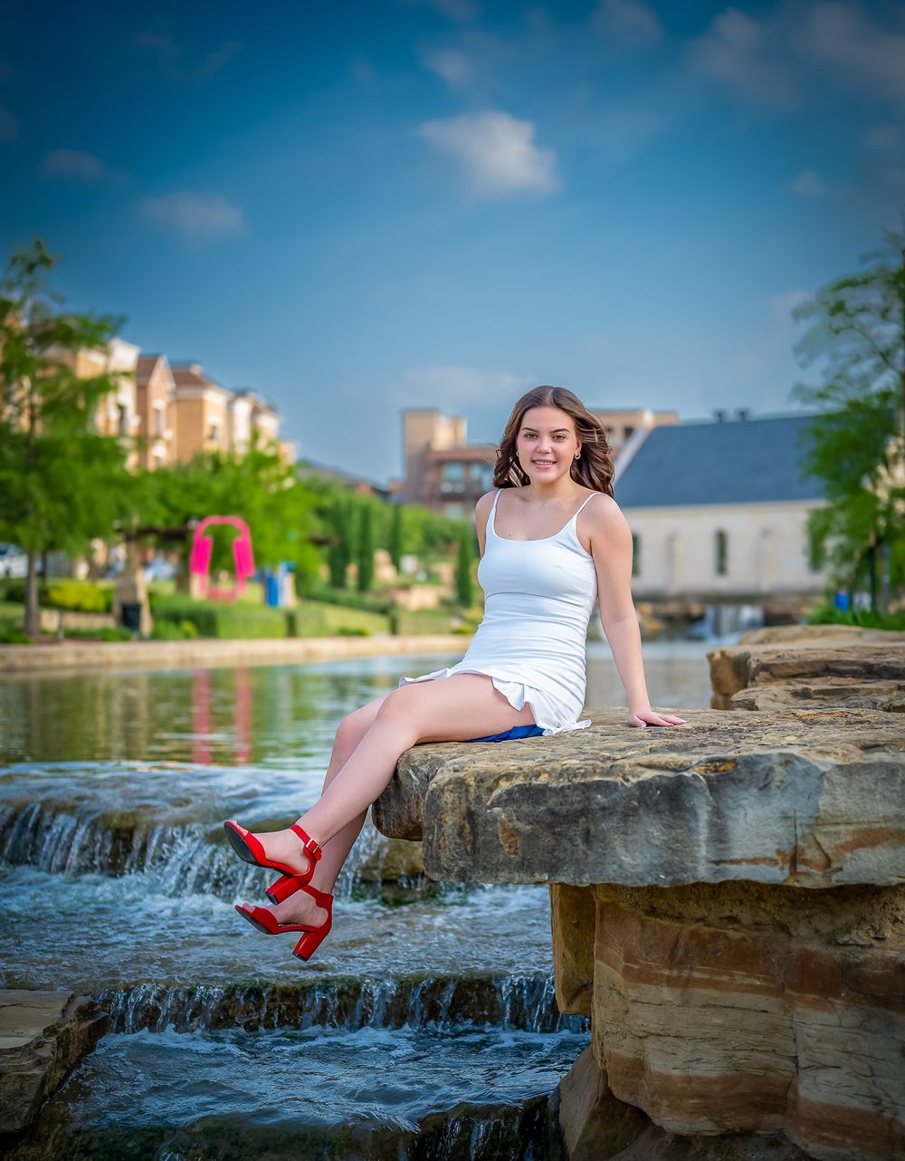 Summer senior portrait on stone waterfall steps wearing white dress and red sandals.