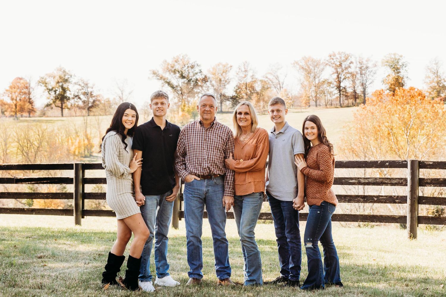 Group portrait of family members standing in front of wooden fence at sunset.