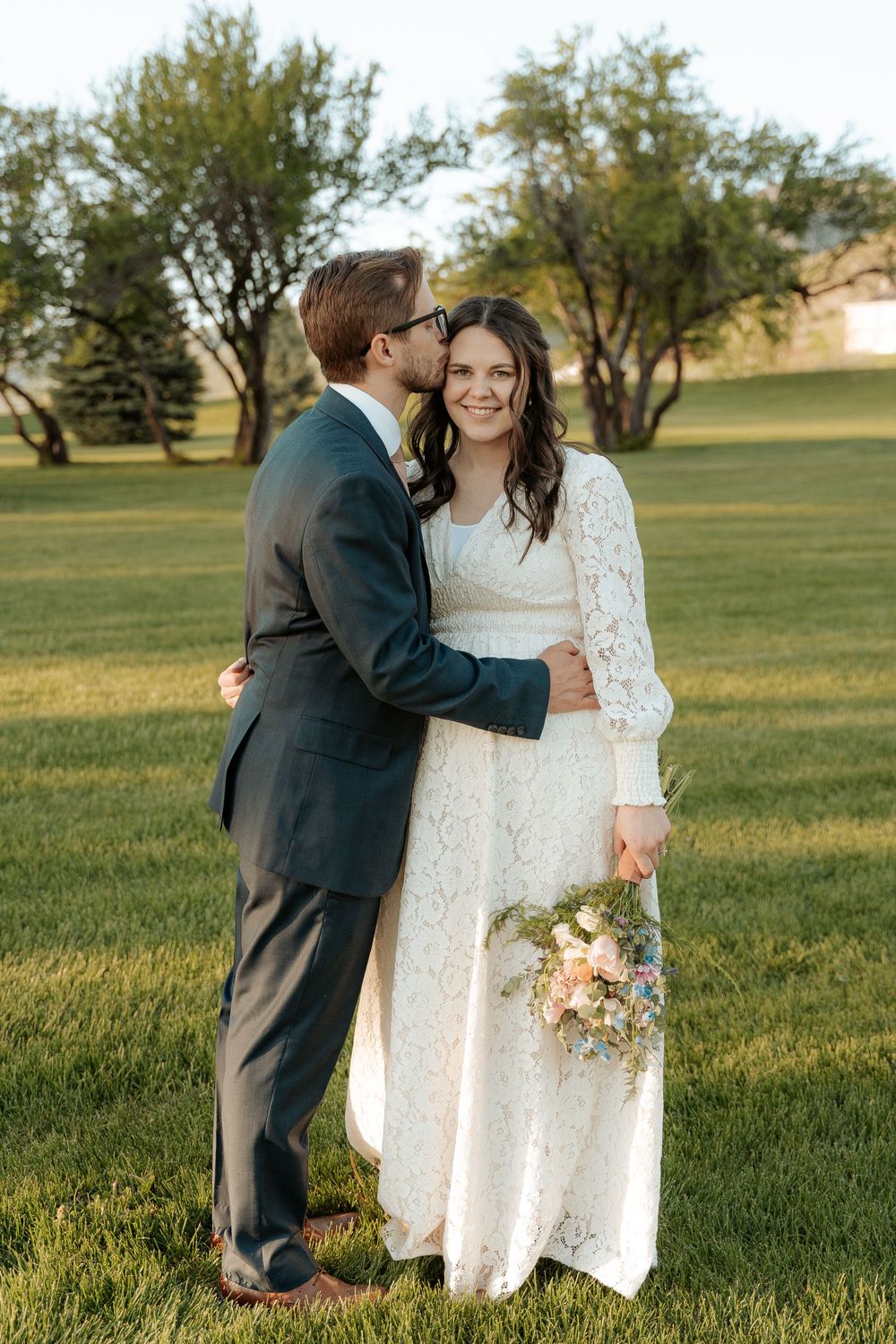 Bride looking into the camera while her groom kisses her forehead during golden hour wedding in Cache Valley UT.