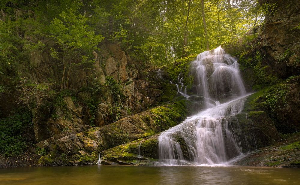Multi-tiered waterfall flowing over moss-covered rocks in a peaceful forest setting.