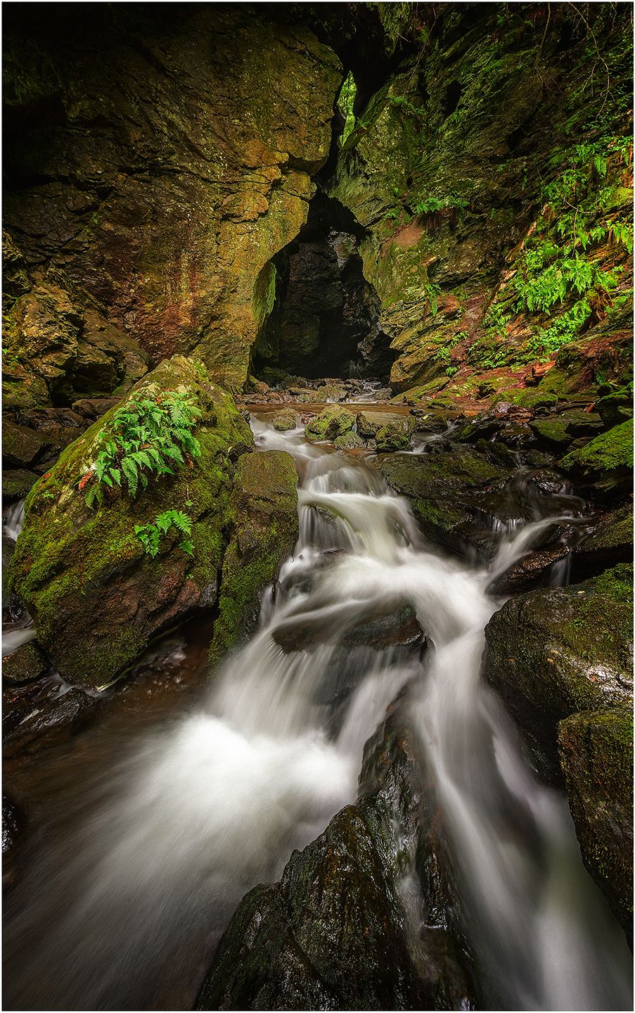 Mossy rocks frame a cascading waterfall flowing through a narrow rocky gorge.