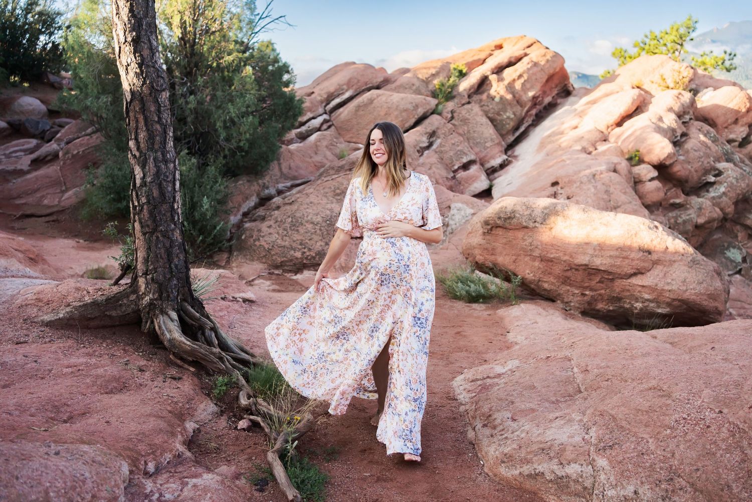 Flowing dress catches wind during maternity shoot among red desert rocks.