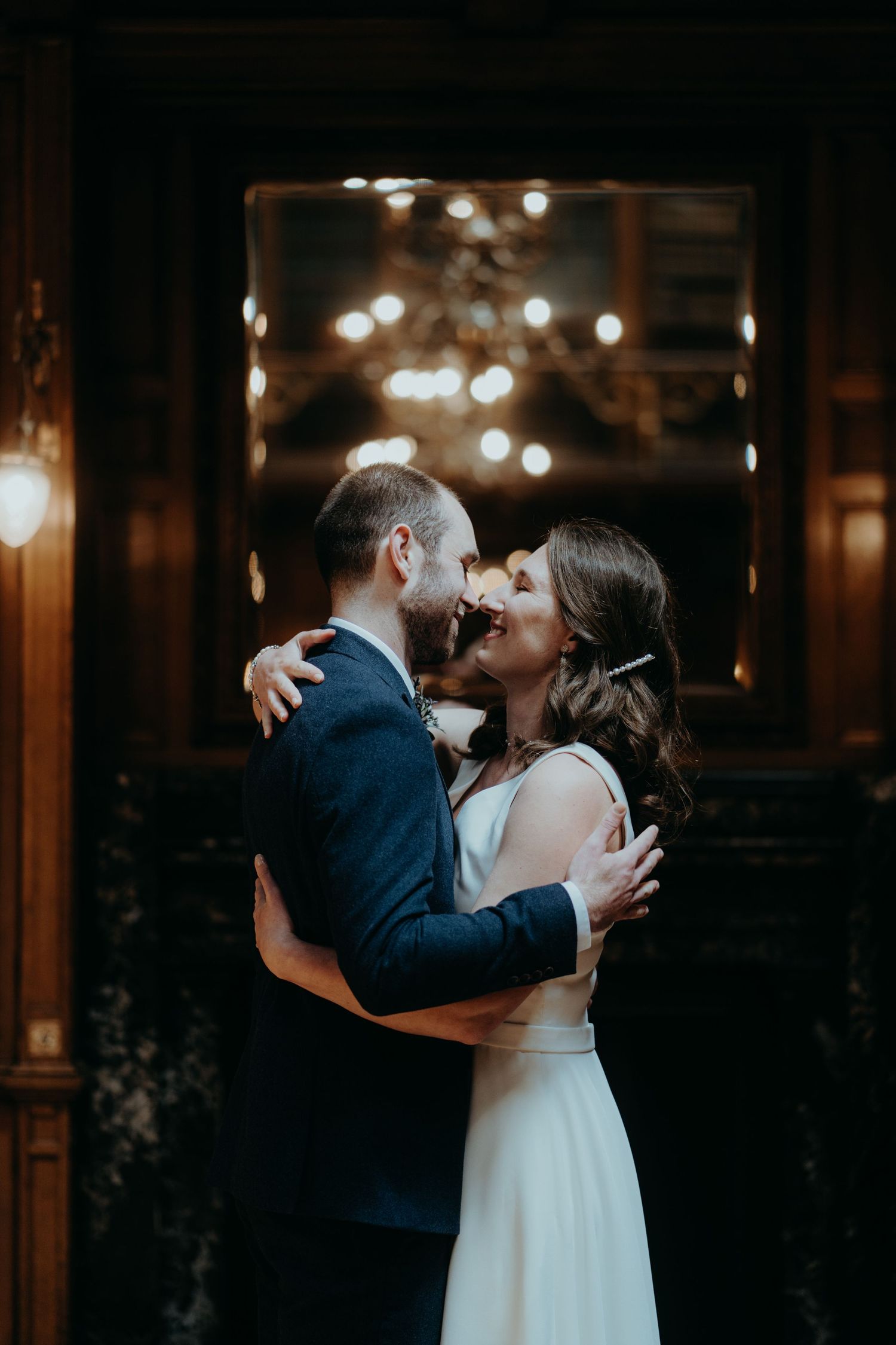 Romantic wedding couple embracing in dark room with bokeh lights in background.