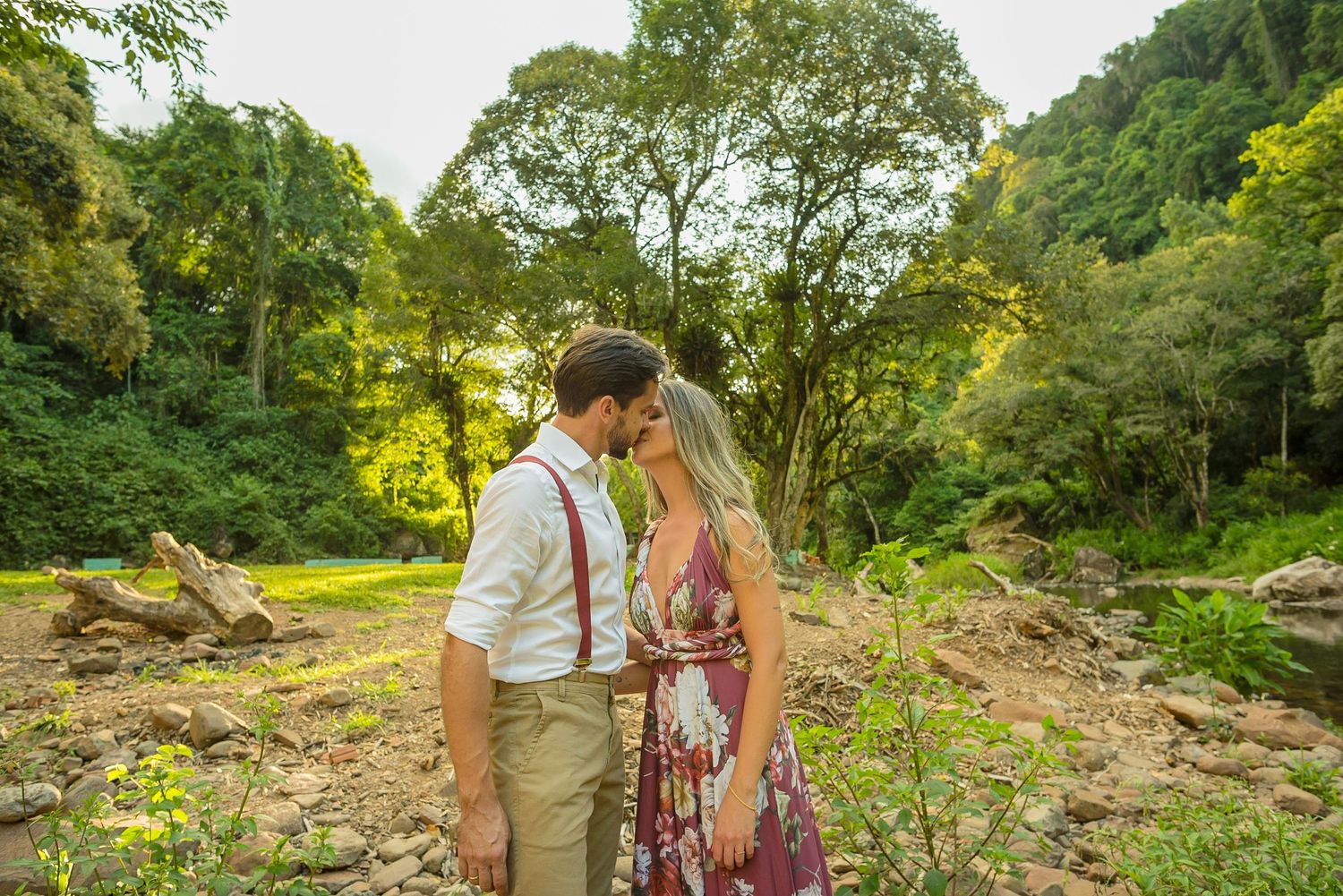 A couple shares an intimate moment against a backdrop of lush green trees and natural scenery.
