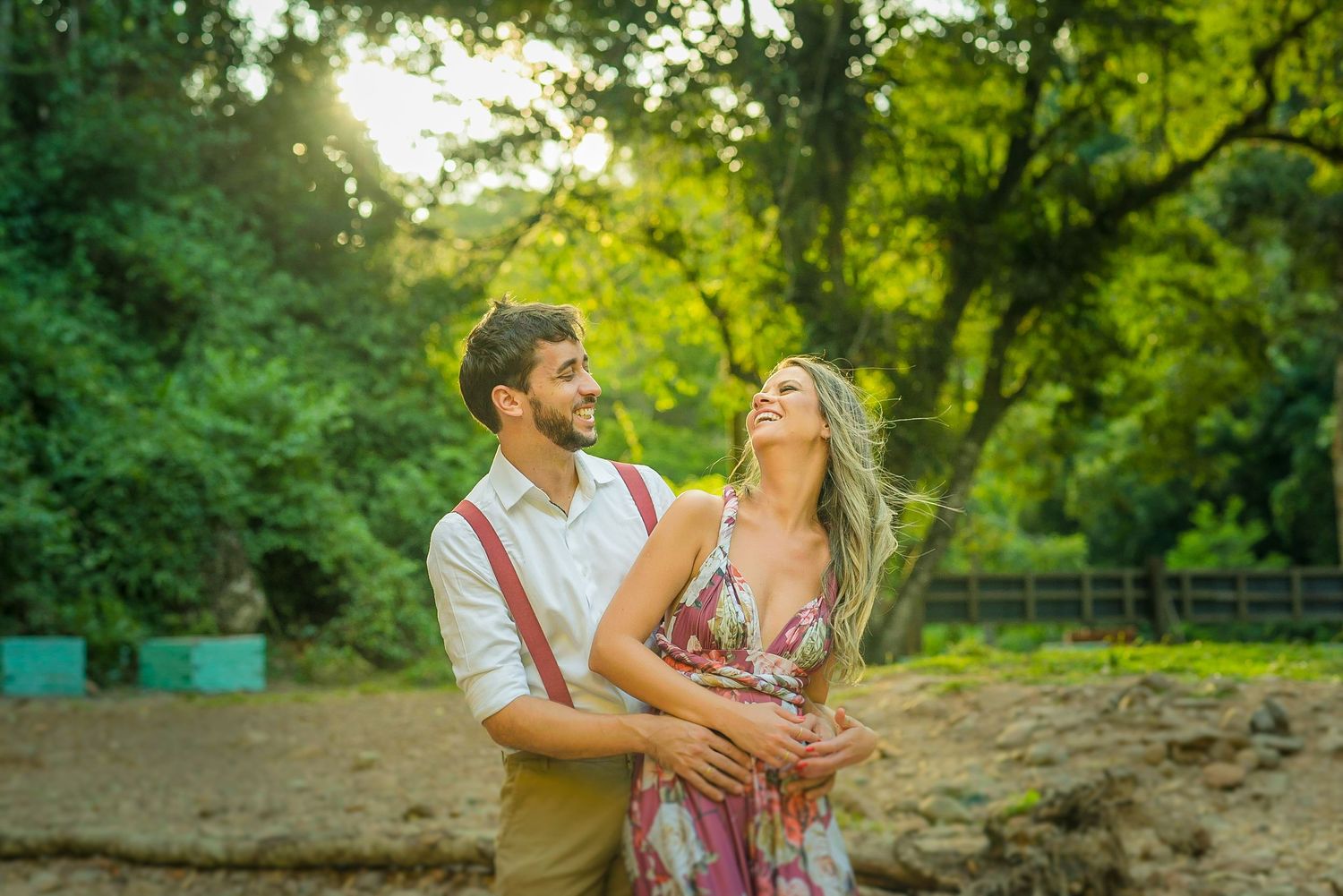 A joyful couple laughs together during a sunset photoshoot in a natural setting.