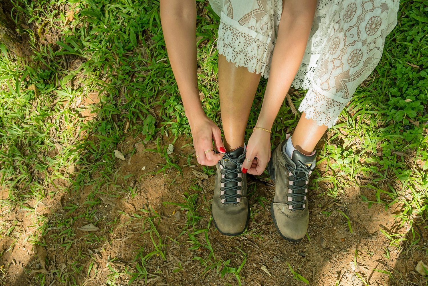 Close-up of hiking boots worn with a lace dress on grass.