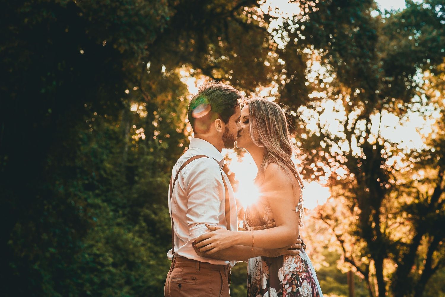 A couple shares an intimate moment at sunset with warm golden light in the background.