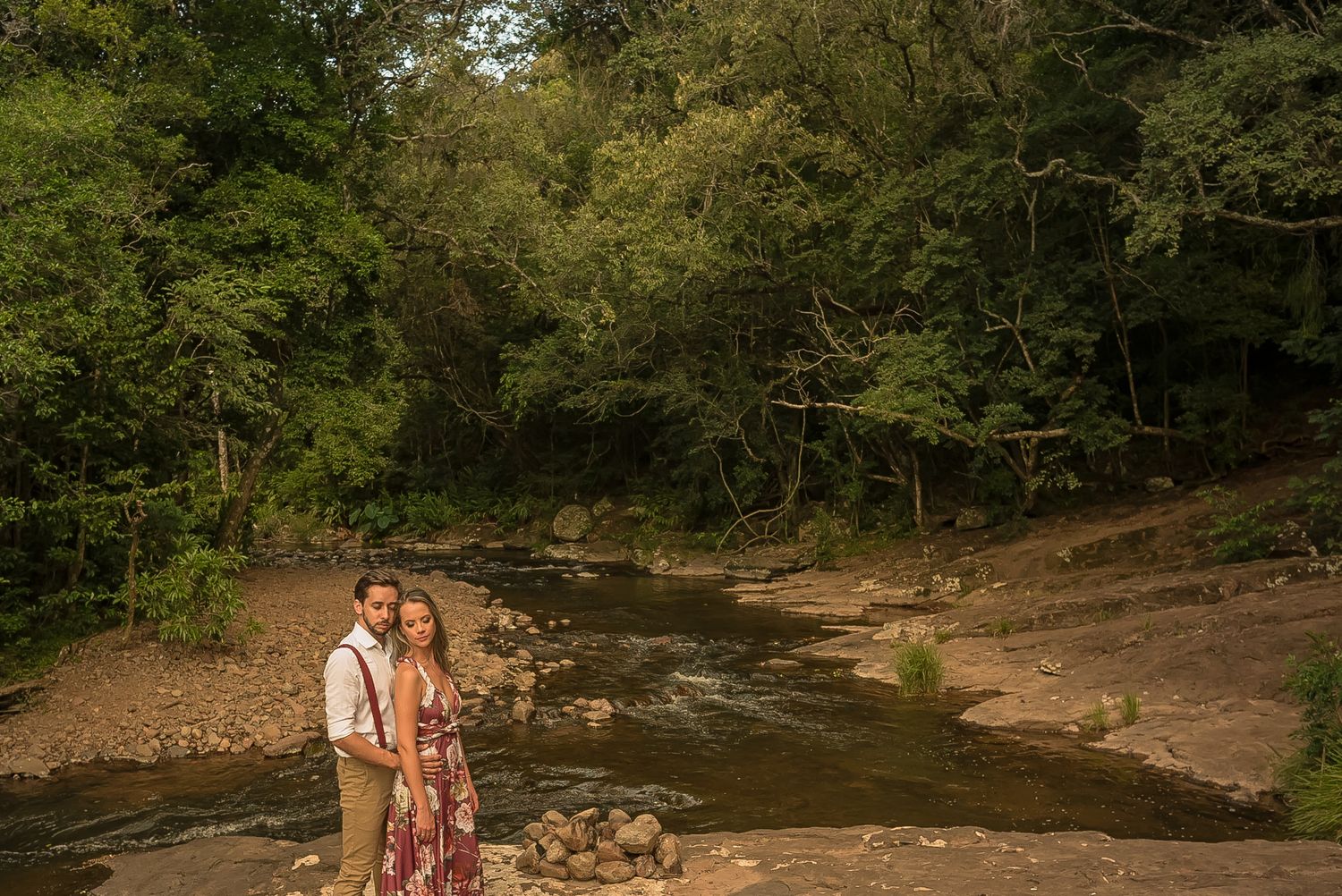A couple standing by a peaceful creek in a wooded area.