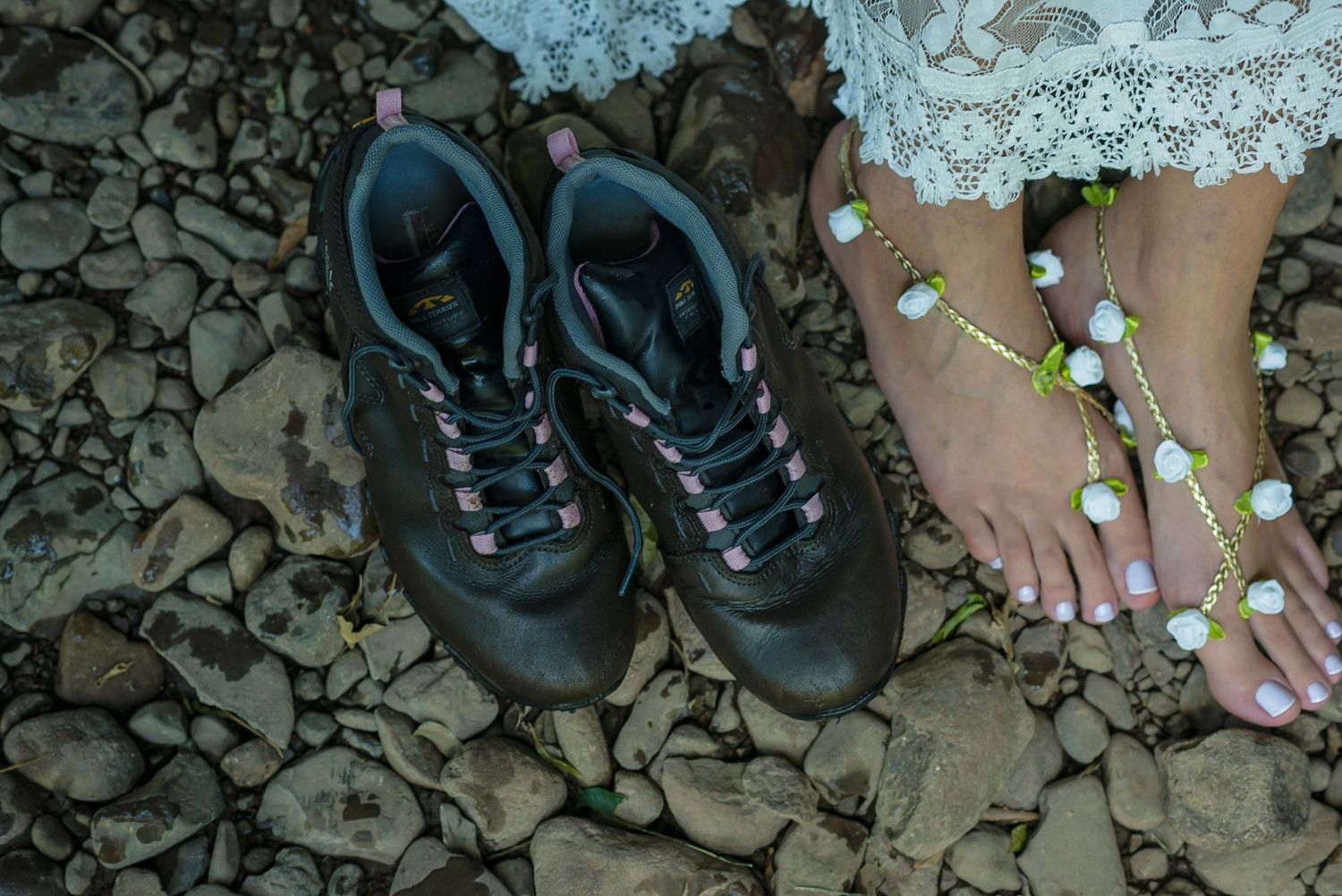 Hiking boots and bare feet with small flowers on rocky ground.