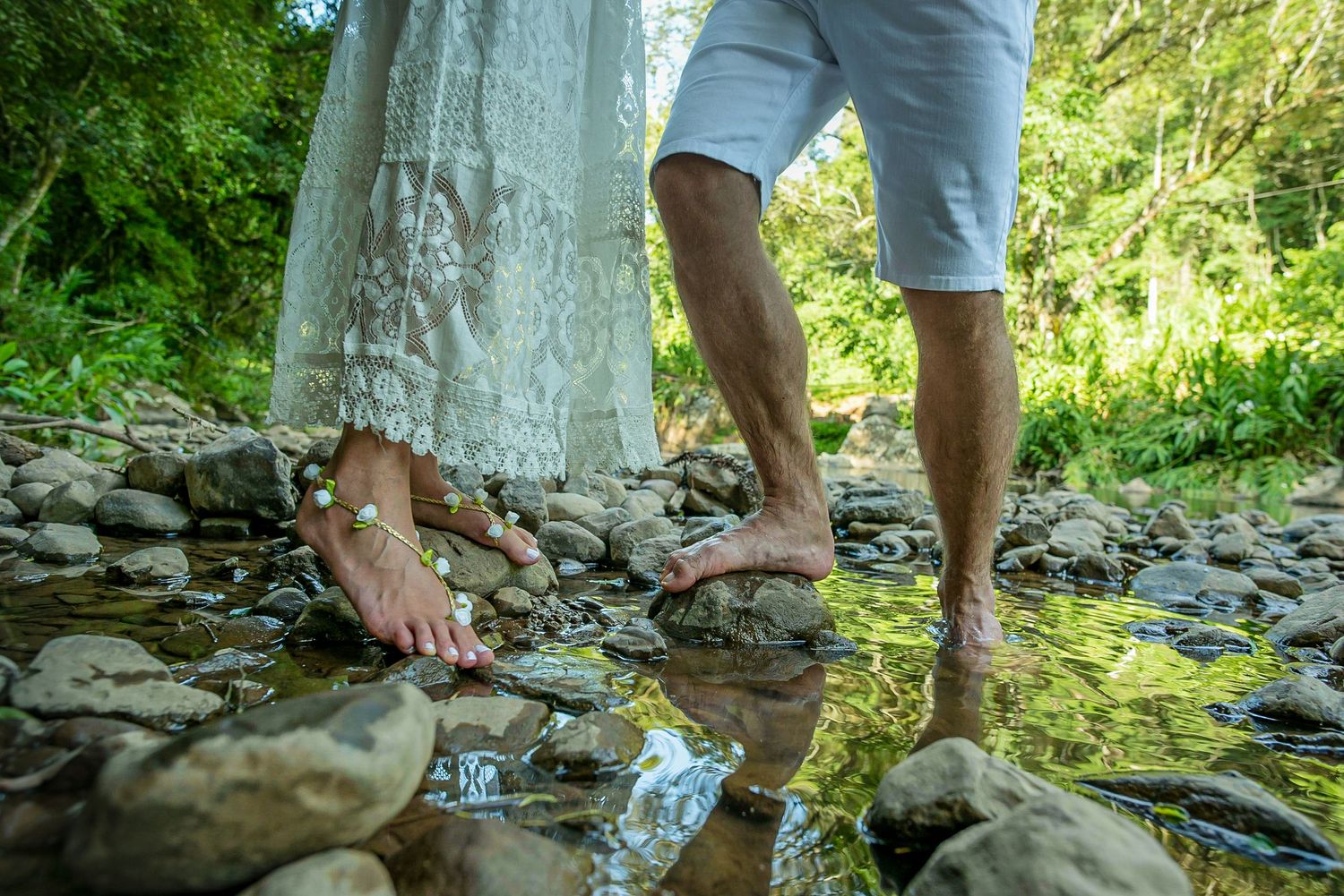 Bare feet and legs standing in shallow stream water on rocky riverbed.