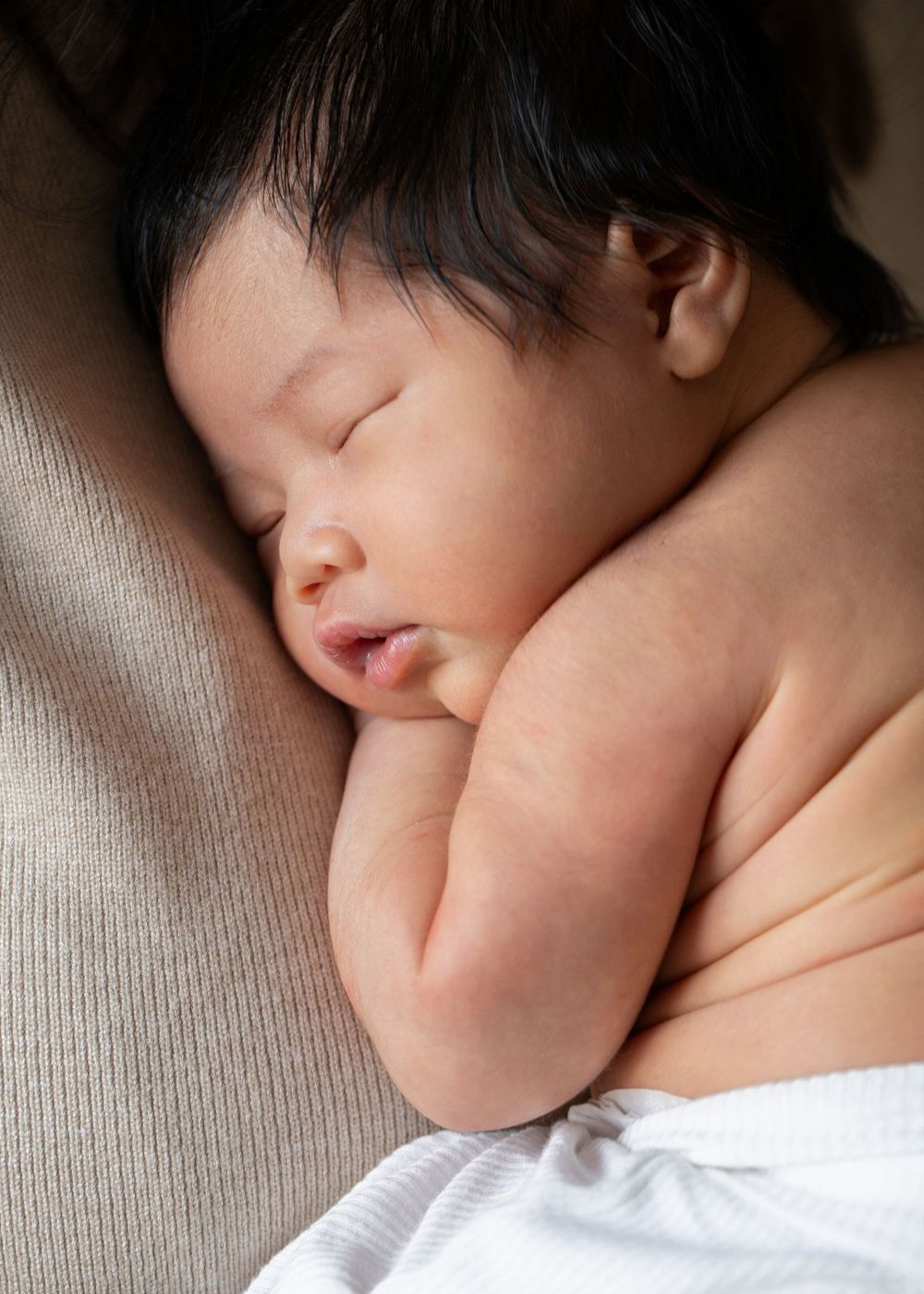 A sleeping baby rests peacefully against a soft gray fabric surface in a series of close-up shots.