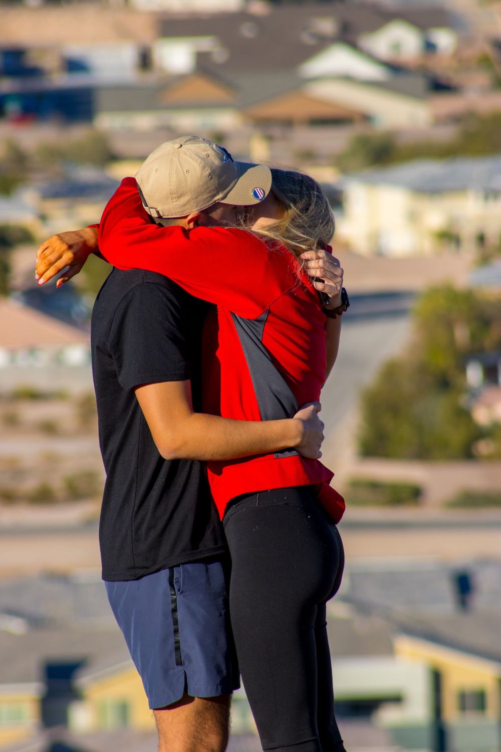 Couple sharing a warm hug on a hilltop viewpoint overlooking a suburban neighborhood at golden hour.